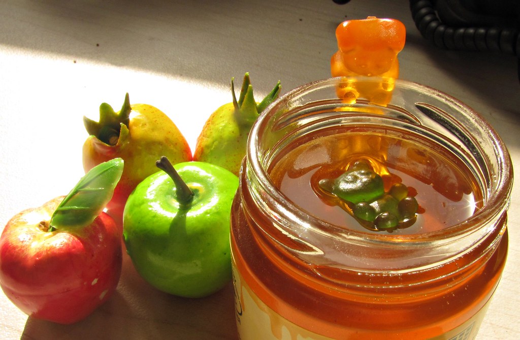 Gummy candy in a jar of honey beside fresh fruit